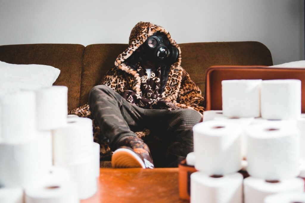 man in mask sitting with a pile of toilet rolls 