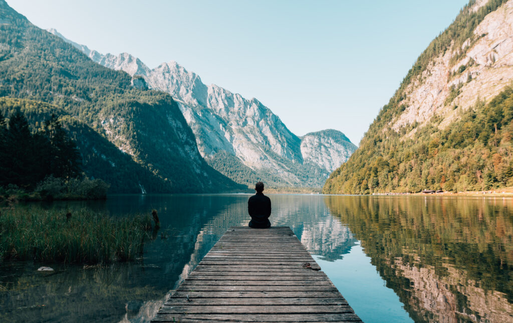 person sitting on the edge of wooden bridge 
